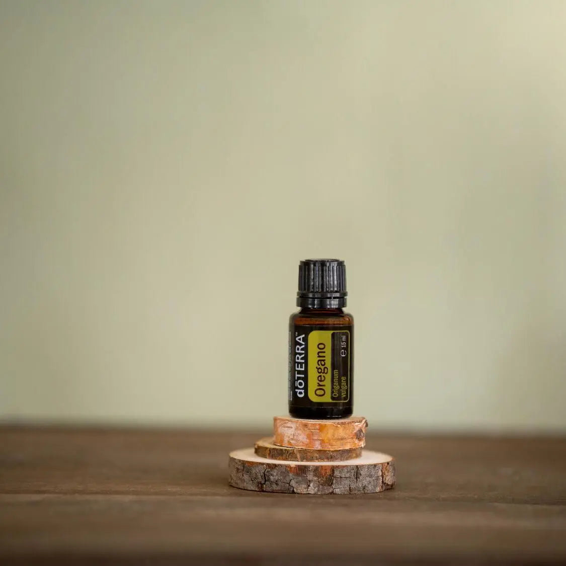 Aceite esencial de Oregano doTERRA 15ml sobre podio de rodajas de abedul apiladas con fondo verde salvia