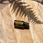 Aceite esencial de Oregano doTERRA 15ml sobre tabla de madera redonda con sombra de palma proyectada al sol