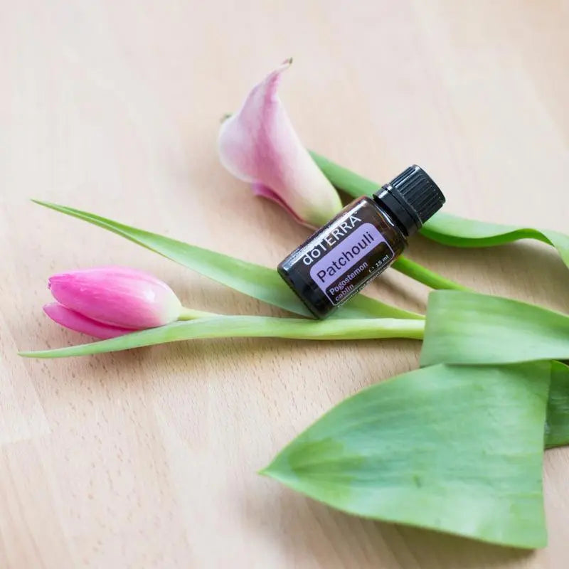 Aceite esencial de Pachulí dōTERRA 15ml sobre madera clara con dos tulipanes rosas y hojas verdes