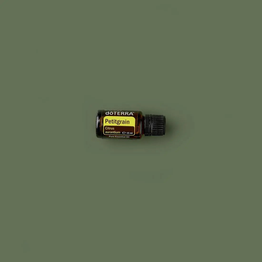 Aceite Esencial Petitgrain dōTERRA 15ml frasco inclinado sobre superficie verde oliva