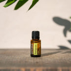 Aceite Esencial Petitgrain dōTERRA 15ml sobre madera rústica con sombra de hoja y luz natural