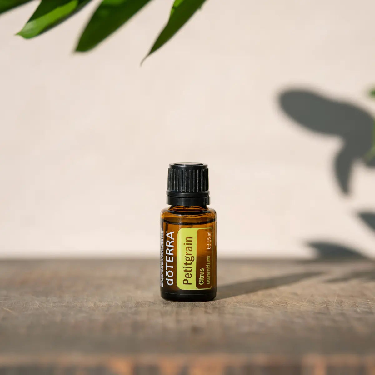 Aceite Esencial Petitgrain dōTERRA 15ml sobre madera rústica con sombra de hoja y luz natural