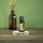 Aceite Esencial Petitgrain dōTERRA 15ml sobre rodaja de tronco con difusor y fondo verde musgo
