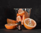 Aceite esencial de pomelo dōTERRA 15ml entre mitades de pomelo exprimido y jarra de vidrio con gajos de pomelo, fondo negro dramático