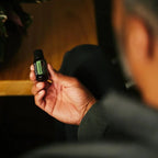 Hombre de pelo gris sujetando el Aceite Esencial de Romero dōTERRA 15ml con iluminación interior cálida y ámbar, visto de espaldas
