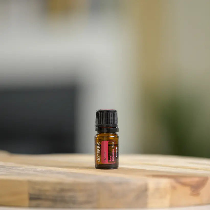 Frasco de aceite esencial de Rosa dōTERRA 5ml sobre tabla de madera natural, fondo neutro desenfocado