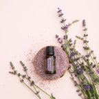 Frasco del Aceite Esencial de Salvia Romana dōTERRA 15ml sobre cuenco de madera con sal de baño rosa, ramas de lavanda fresca alrededor, fondo rosa pálido