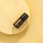 Aceite esencial de Sándalo Indiano dōTERRA 5ml sobre disco de madera natural clara sobre fondo amarillo cálido, composición minimalista