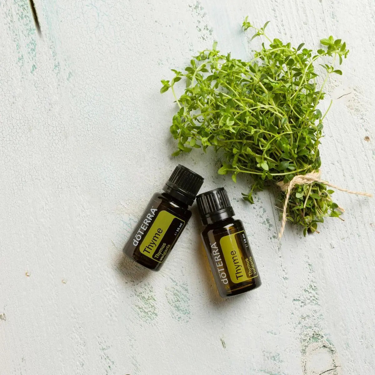 Dos frascos de aceite esencial de Tomillo dōTERRA 15ml junto a manojo de tomillo fresco atado con cordel, tabla de madera vintage