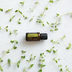Aceite esencial de Tomillo dōTERRA 15ml rodeado de ramas de tomillo fresco esparcidas sobre superficie de mármol blanco, vista cenital