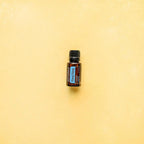 Frasco del Aceite Esencial de Ylang Ylang dōTERRA 15ml centrado sobre fondo liso amarillo crema, composición minimalista