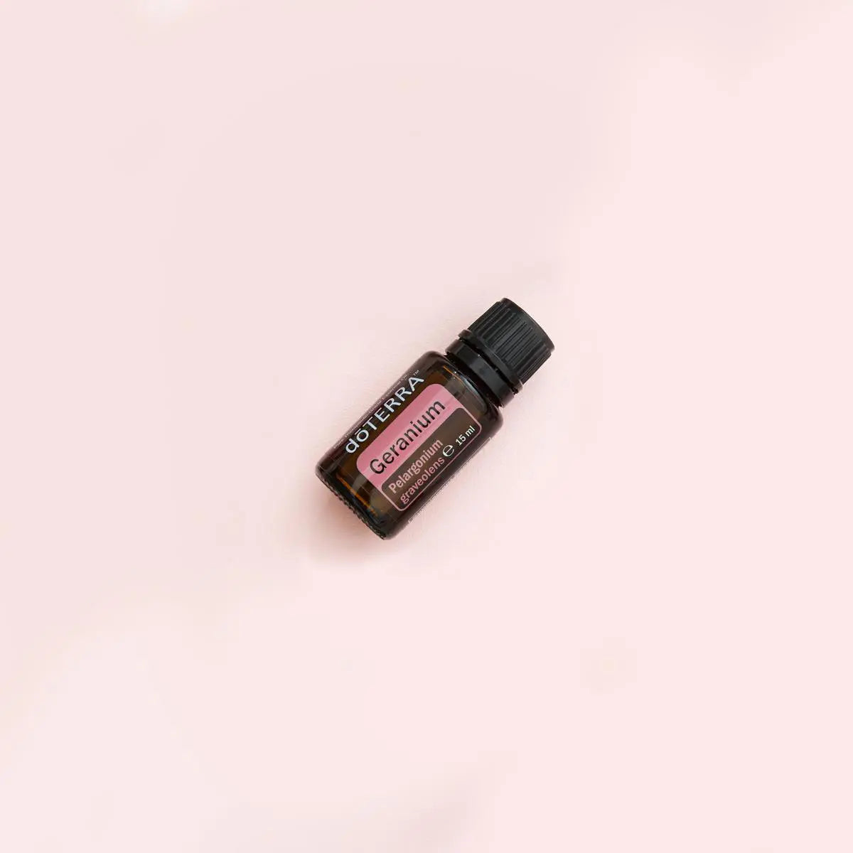 Aceite esencial de geranio dōTERRA 15ml — frasco inclinado sobre fondo rosa pastel