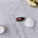 Aceite esencial de geranio dōTERRA 15ml — frasco sobre mármol con discos de algodón y espejo dorado
