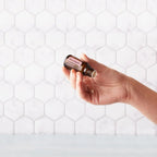 Aceite esencial de geranio dōTERRA 15ml — mano sosteniendo el frasco sobre azulejos hexagonales blancos