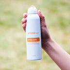 After Sun dōTERRA spray 170g — mano sosteniendo el frasco con fondo de hierba verde