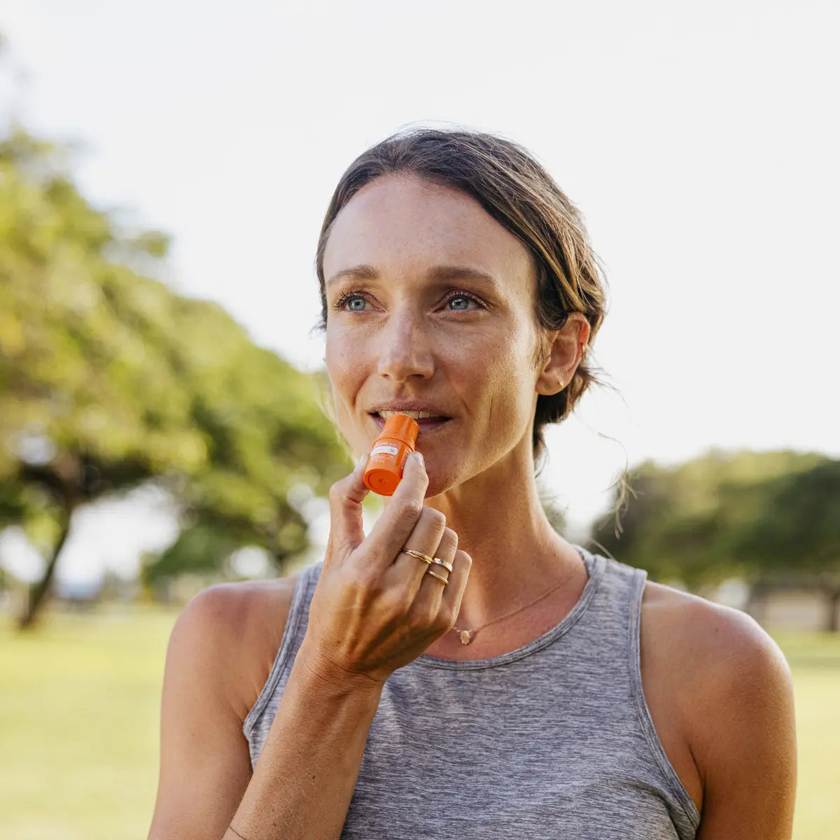 Bálsamo labial Sun dōTERRA SPF 15 — mujer aplicando en los labios en parque exterior