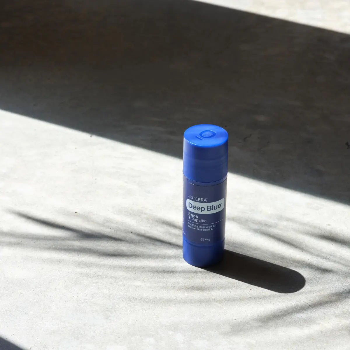 Barra Deep Blue Copaiba dōTERRA sobre superficie de piedra con sombras y luz solar