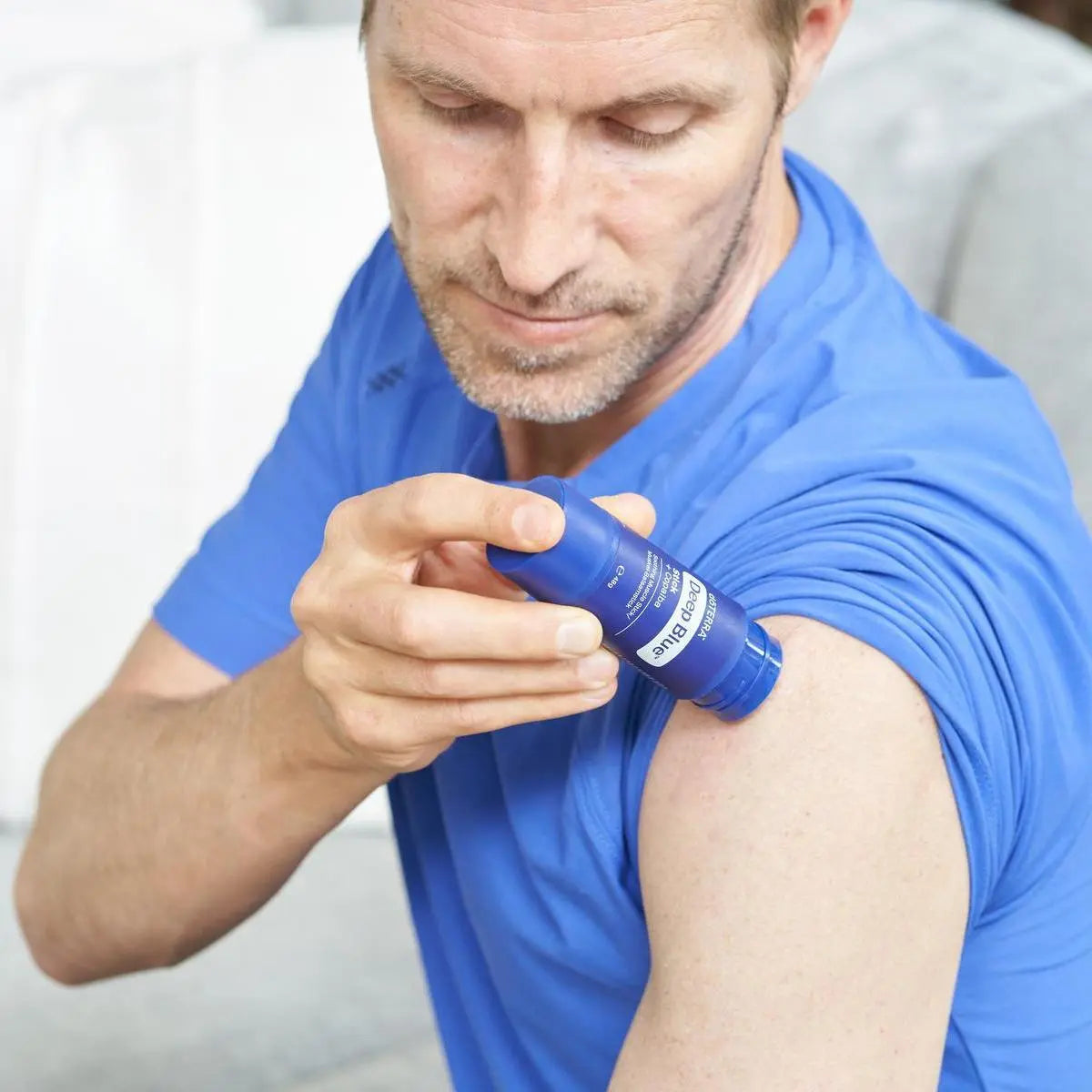 Hombre con polo azul aplicando barra Deep Blue dōTERRA en el hombro en primer plano