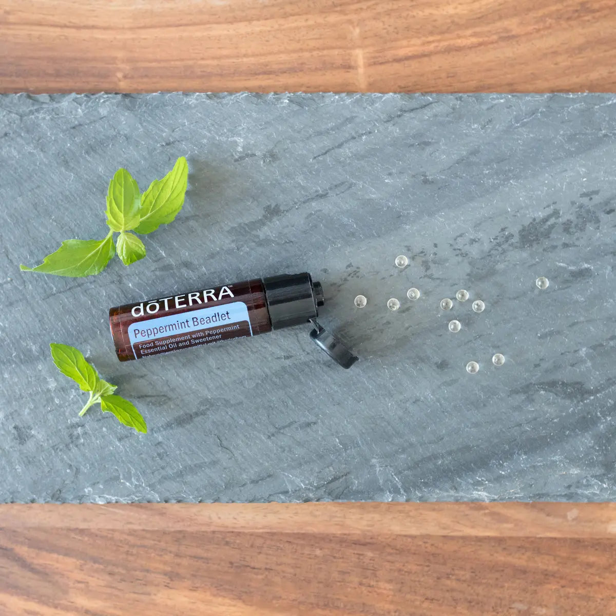 Bolitas Menta Piperita Beadlets dōTERRA sobre pizarra gris con hojas de menta y perlas cenital