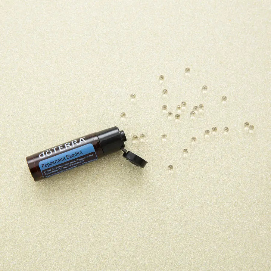 Peppermint Beadlets dōTERRA con perlas esparcidas sobre superficie dorada vista cenital