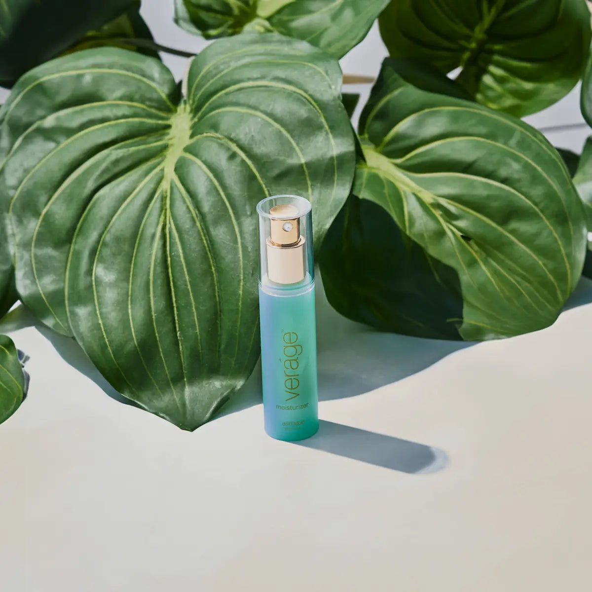 Crema Hidratante Veráge dōTERRA 30ml — frasco junto a plantas fondo beige