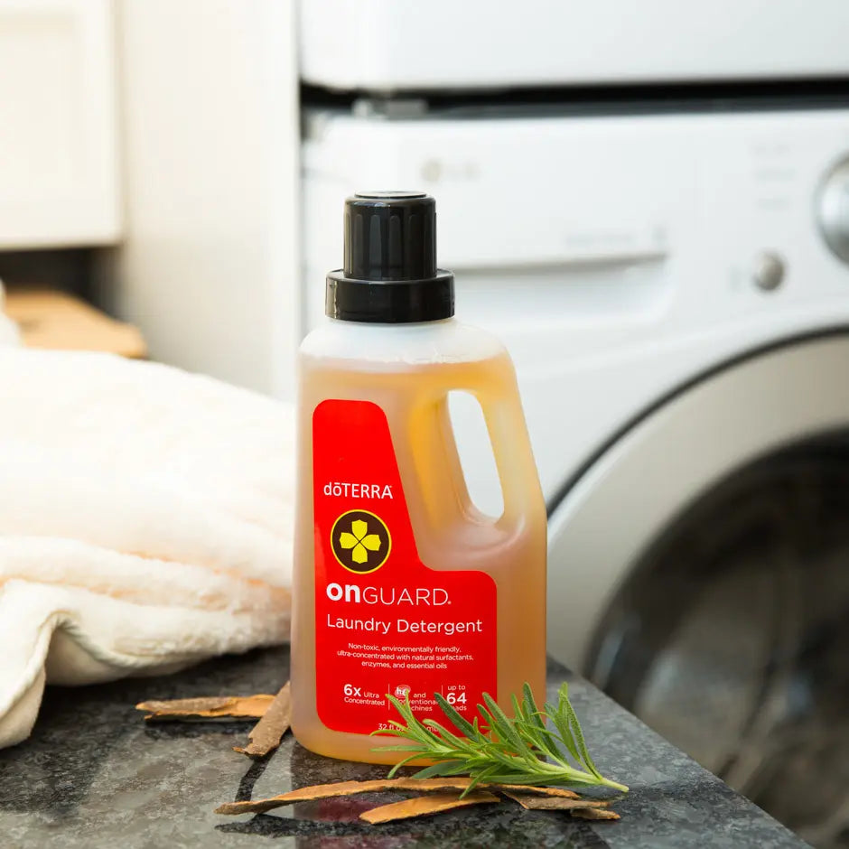 Detergente para lavadora On Guard dōTERRA 947ml — frasco junto a romero y corteza de naranja