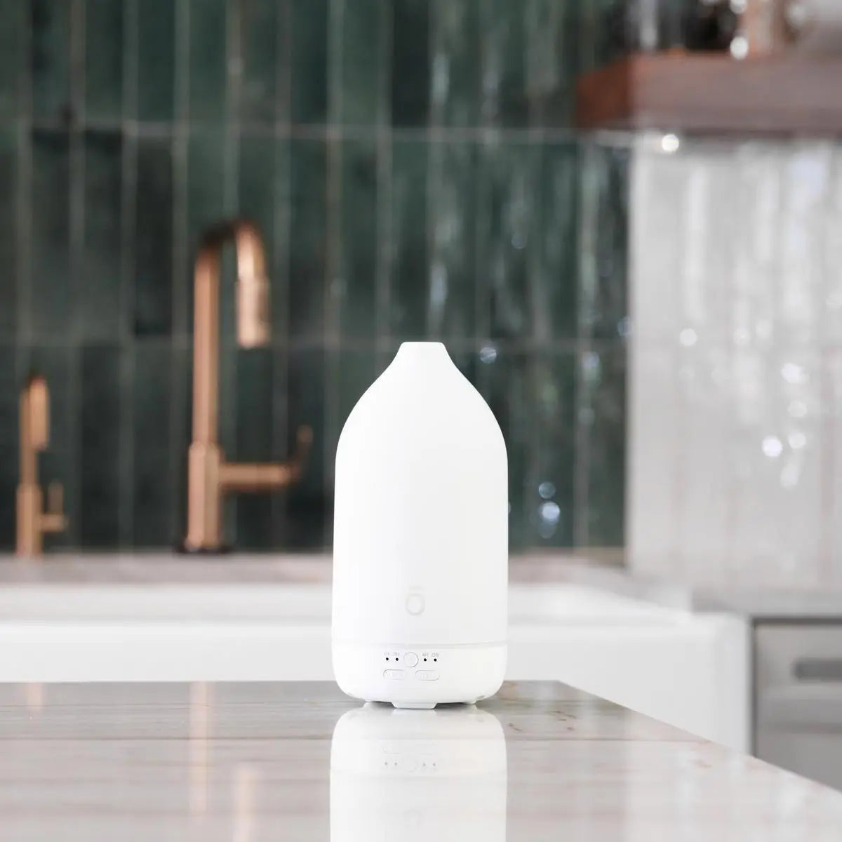 Difusor Laluz dōTERRA blanco en cocina de mármol con grifo de cobre y azulejos verdes