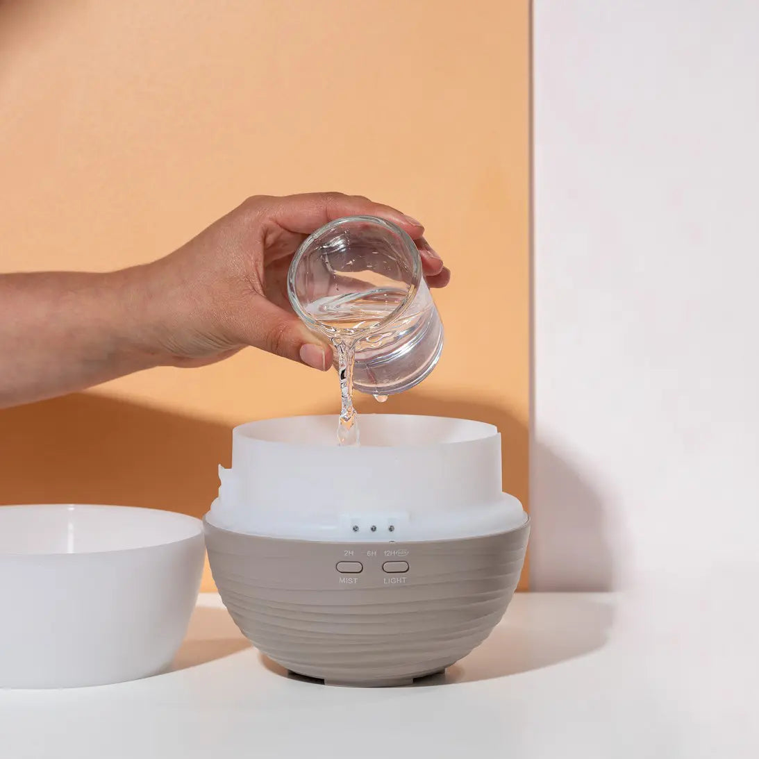 Mano llenando de agua el Difusor Pétalo dōTERRA sobre fondo naranja