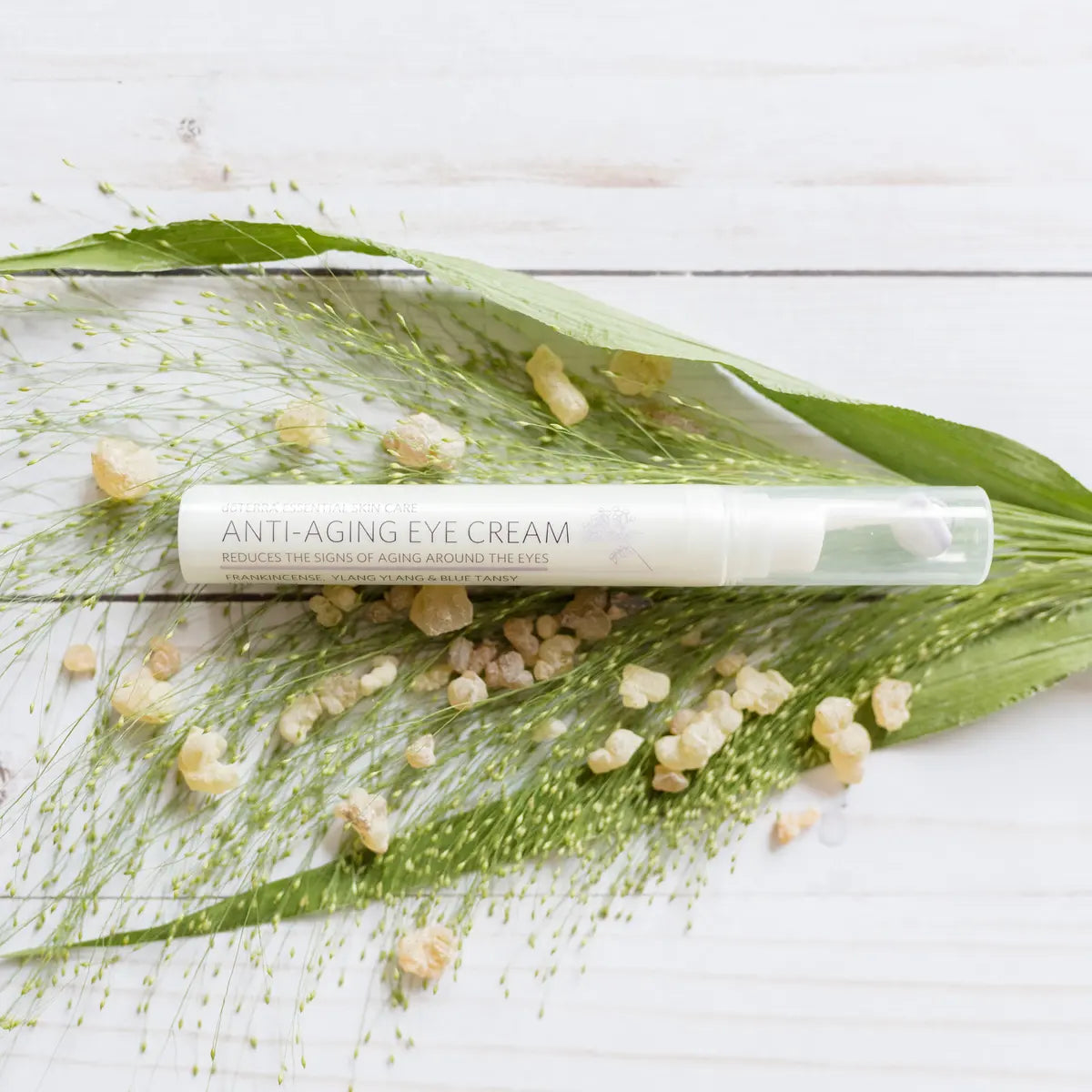 Envase de crema para el contorno de ojos dōTERRA Anti-Aging Eye Cream sobre hoja verde y resina de incienso en fondo de madera clara.