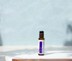 Frasco roll-on dōTERRA Calmer Touch 10ml destapado sobre bandeja de mármol con sombras de hojas y fondo azul suave.