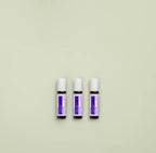 Tres frascos roll-on dōTERRA Calmer Touch 10ml alineados lado a lado sobre fondo verde menta pastel.