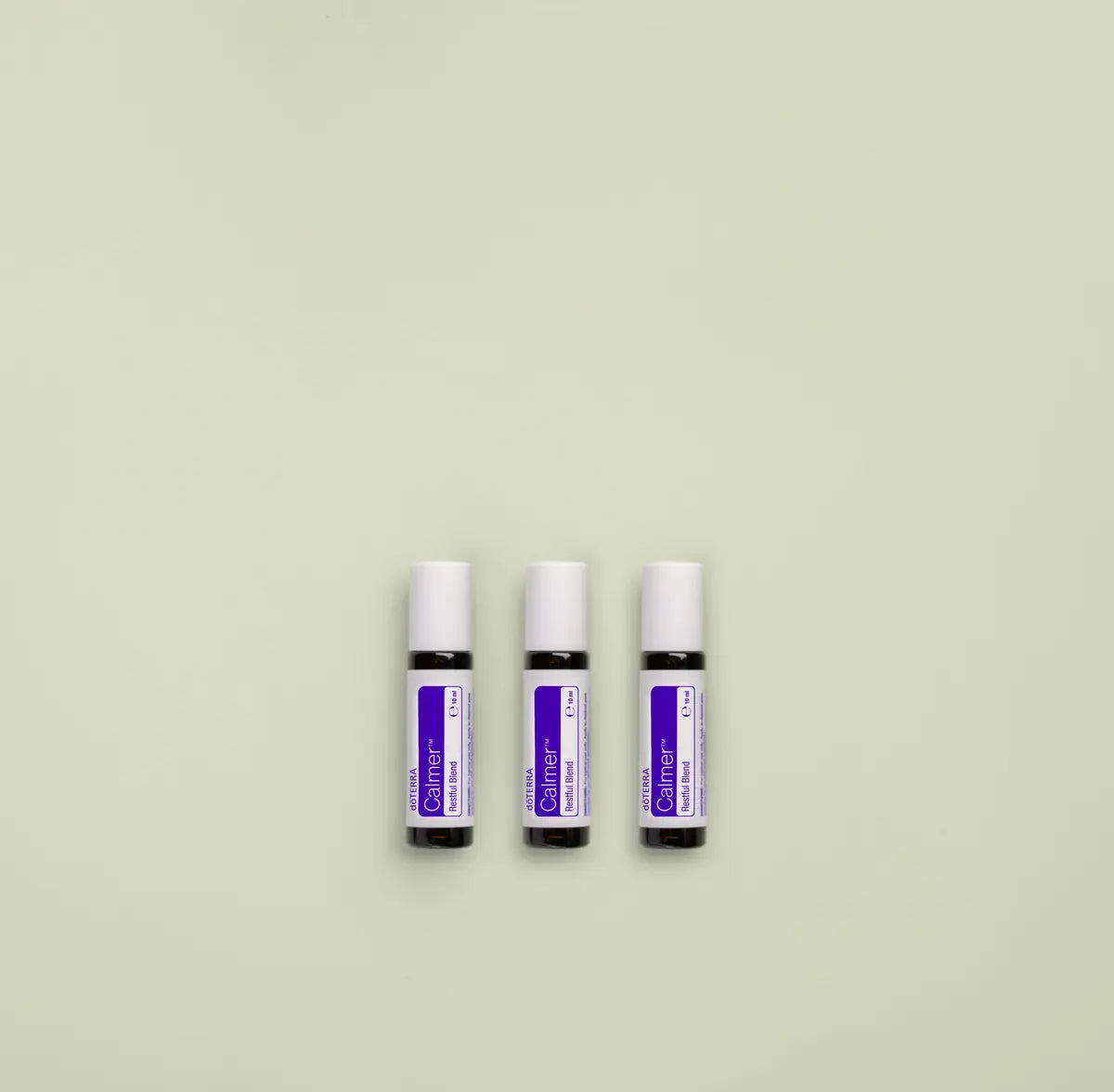 Tres frascos roll-on dōTERRA Calmer Touch 10ml alineados lado a lado sobre fondo verde menta pastel.