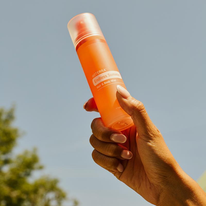 Mano sosteniendo bruma doTERRA Endless Summer Hair & Body Mist 100 ml al aire libre
