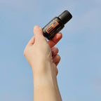 Mano sosteniendo aceite esencial doTERRA Endless Summer Sunshine Blend 15 ml contra el cielo azul