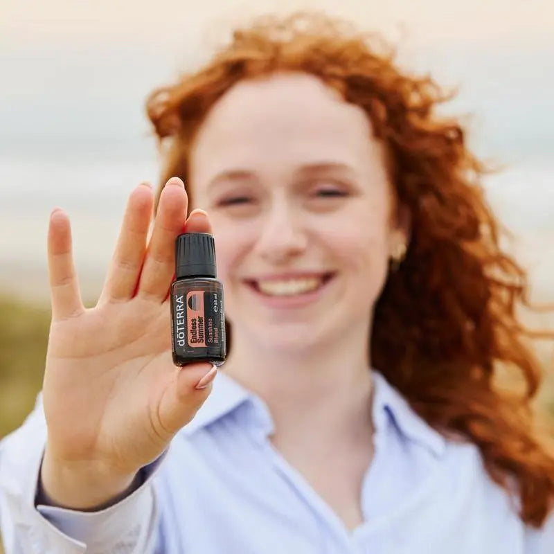 Mujer sosteniendo aceite esencial doTERRA Endless Summer Sunshine Blend 15 ml al aire libre