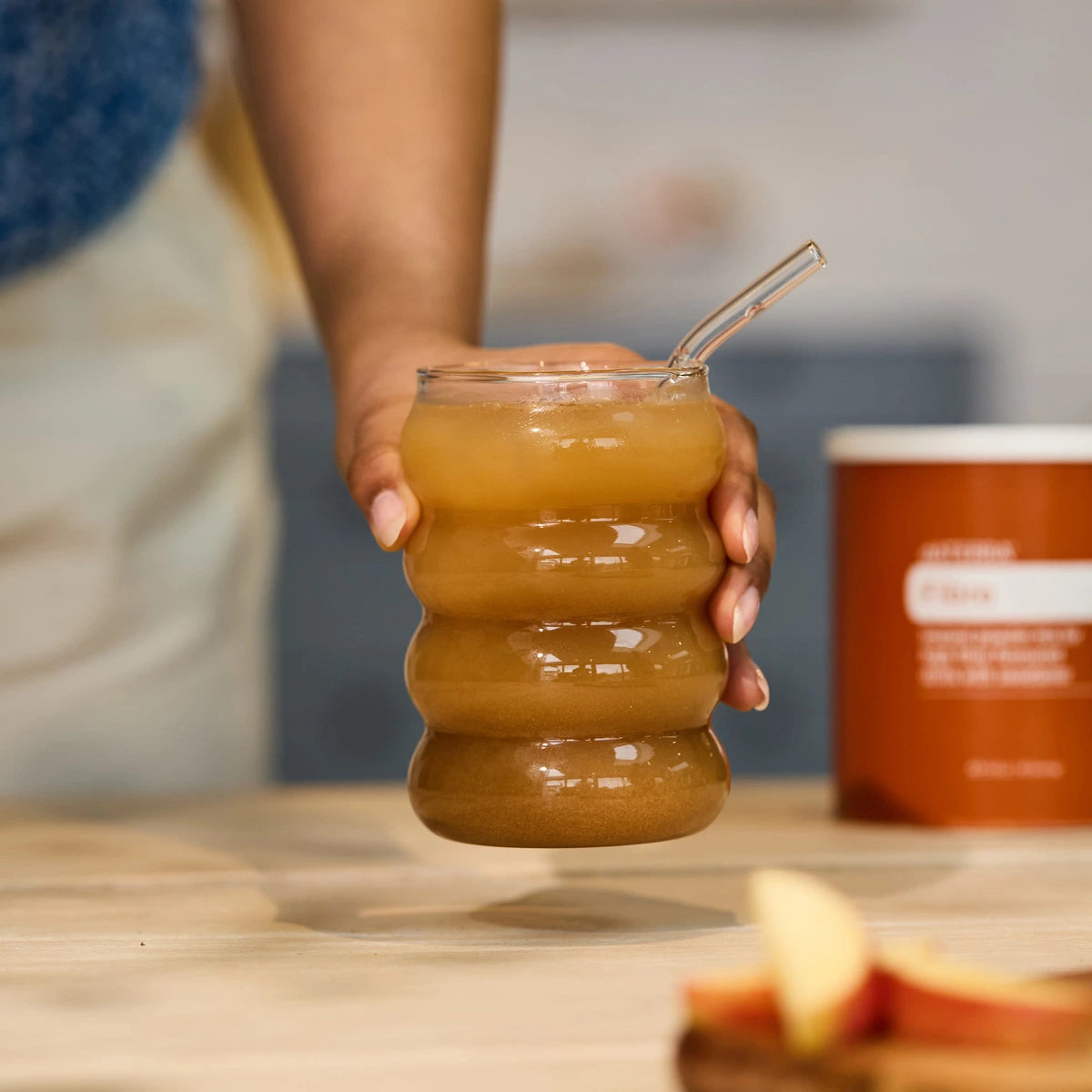 Mano sosteniendo vaso con bebida de Fibra doTERRA preparada con bote naranja al fondo
