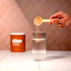 Mano vertiendo cacito de polvo Fibra doTERRA en vaso de agua con bote naranja al fondo
