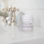 Tarro abierto de dōTERRA Hydrating Cream 48g con la tapa apoyada sobre la encimera de un lavabo de baño.