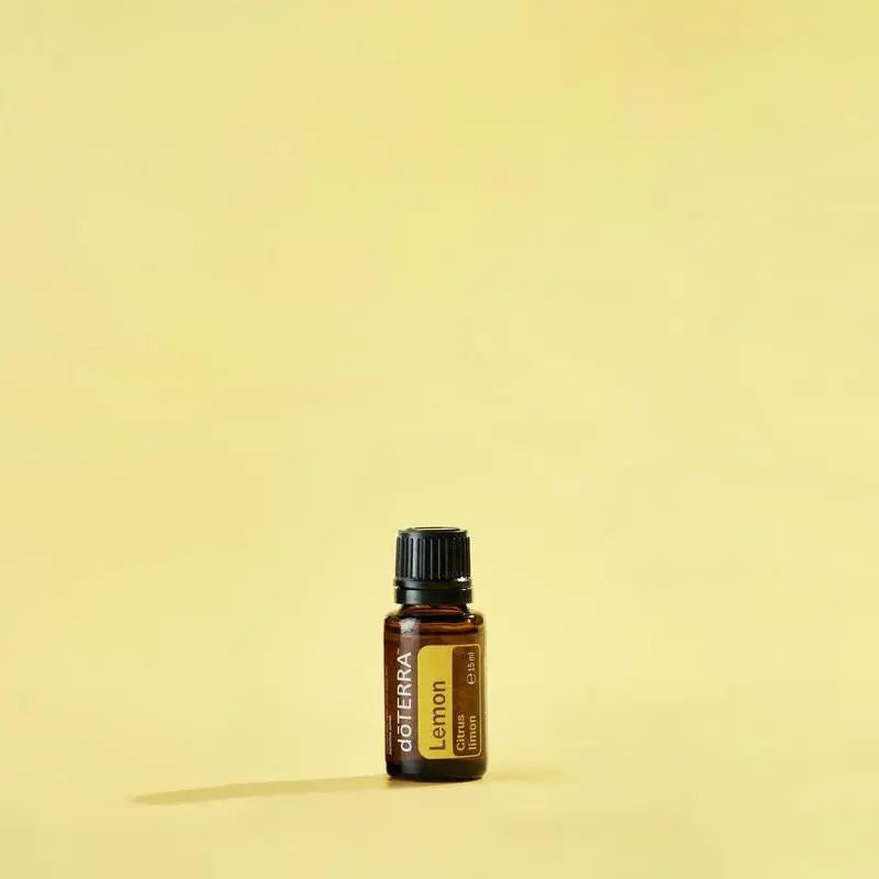 Frasco de aceite esencial dōTERRA Lemon 15ml centrado sobre fondo amarillo claro.