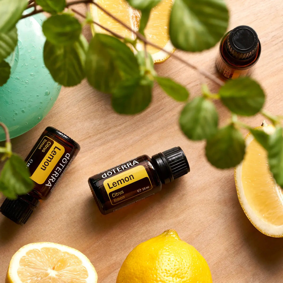 Frascos de aceite esencial dōTERRA Lemon 15ml tumbados sobre mesa de madera rodeados por rodajas de limón y hojas verdes.