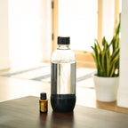 Frasco de aceite esencial dōTERRA Lemon 15ml junto a una botella transparente con agua sobre mesa de madera.