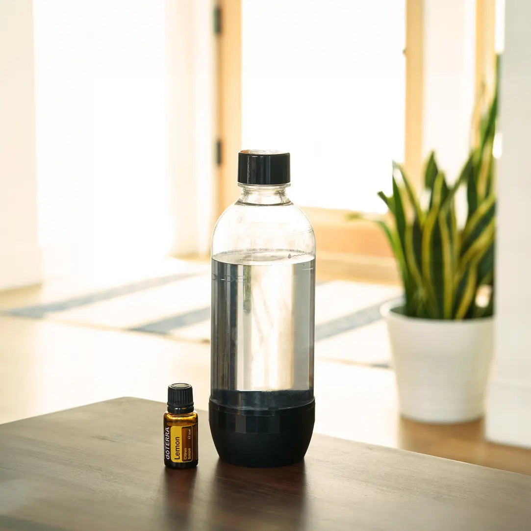 Frasco de aceite esencial dōTERRA Lemon 15ml junto a una botella transparente con agua sobre mesa de madera.