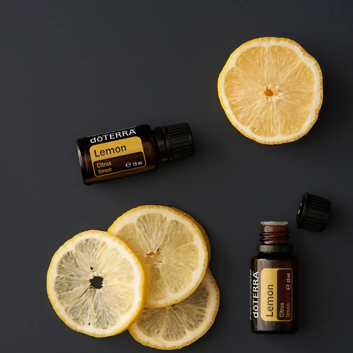 Frascos de dōTERRA Lemon 15ml y rodajas de limón dispuestos sobre un fondo azul oscuro elegante.