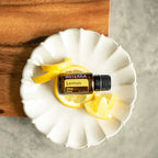 Frasco de aceite esencial dōTERRA Lemon 15ml sobre rodajas y cáscara de limón en un plato de cerámica blanca ondulado.