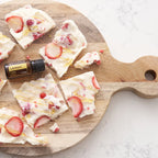 Frasco de dōTERRA Lemon 15ml junto a trozos de snack congelado de yogur con fresas y miel sobre tabla de cortar de madera.