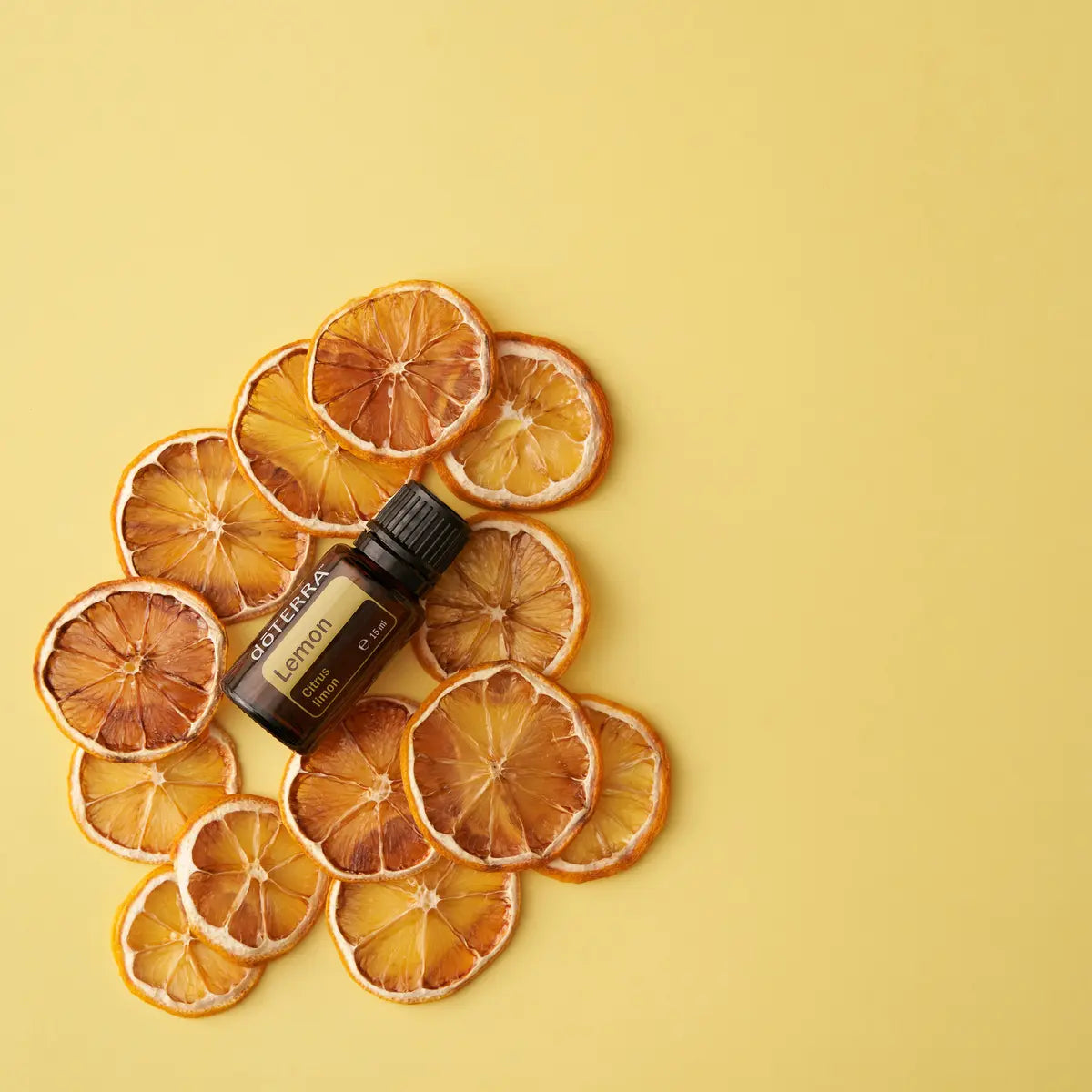 Frasco de aceite esencial dōTERRA Lemon 15ml sobre una composición de rodajas de limón deshidratado en fondo amarillo claro.
