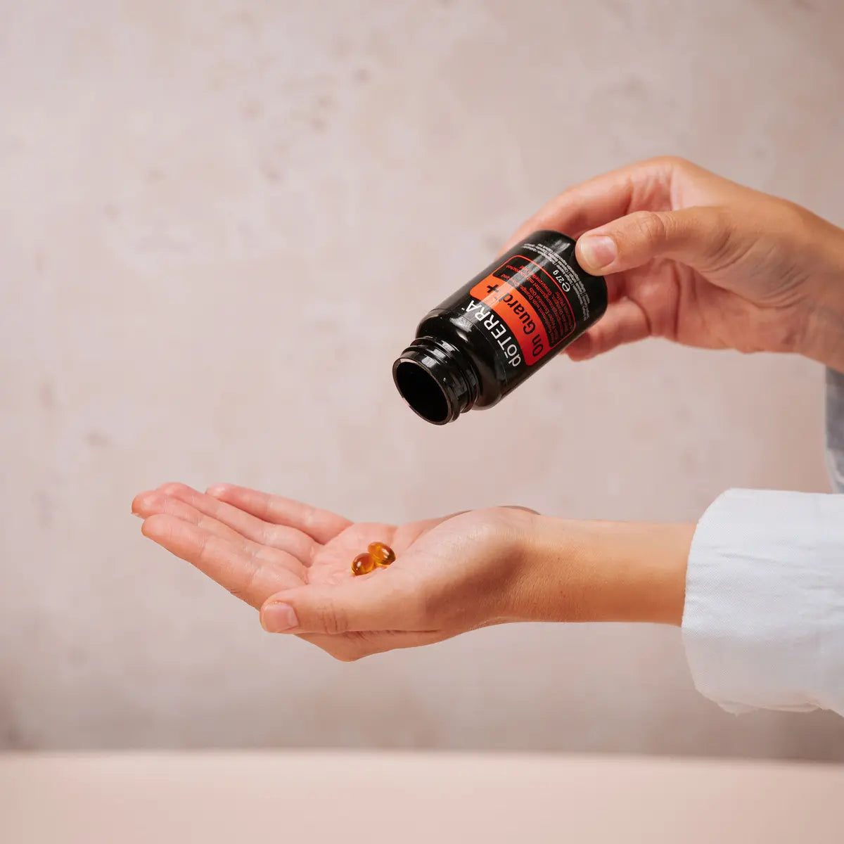 Pessoa a deitar duas cápsulas moles dōTERRA On Guard+ do frasco para a palma da mão.