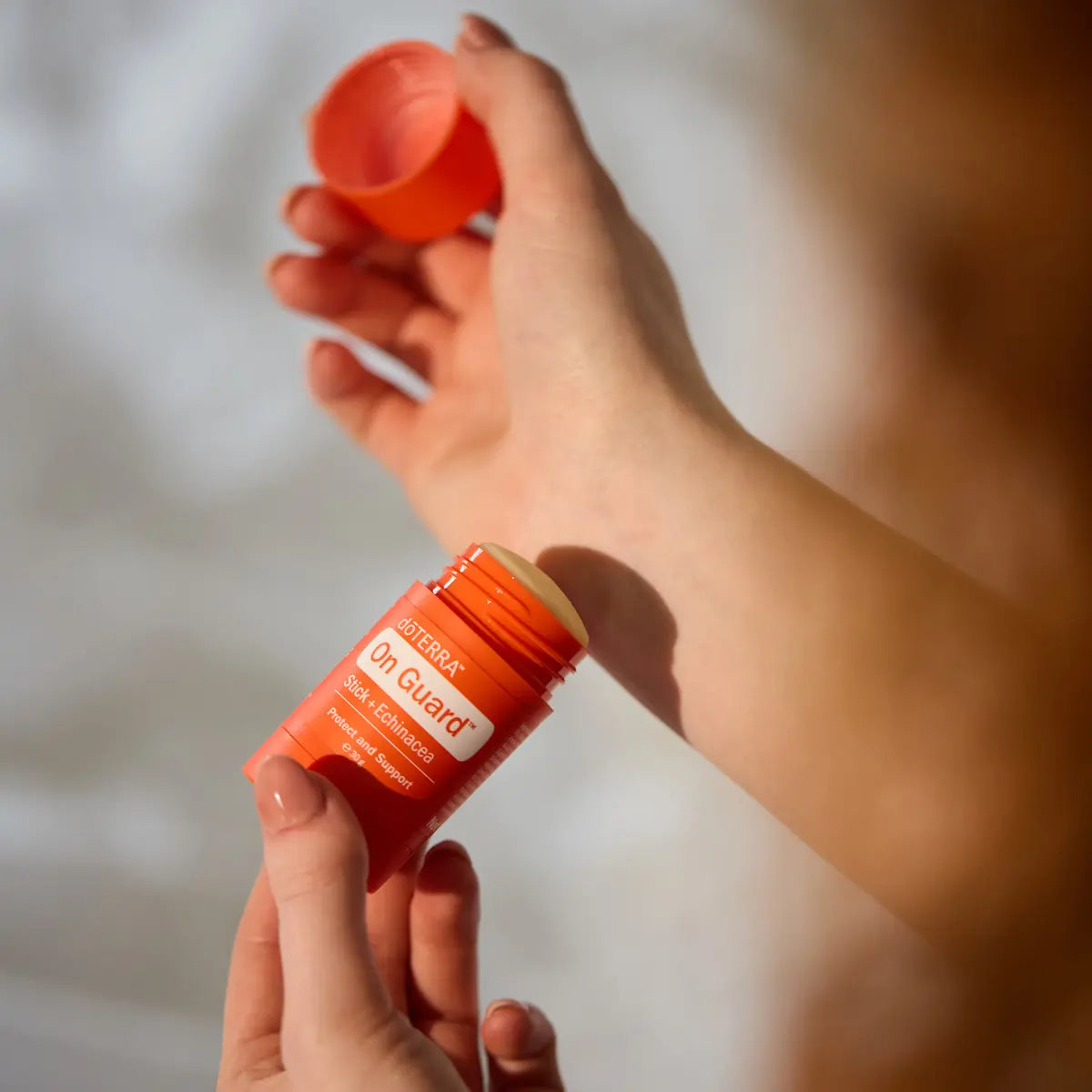Manos aplicando la barra dōTERRA On Guard Stick con Equinácea en la muñeca.