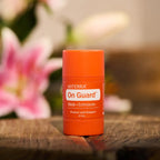 Envase naranja de dōTERRA On Guard Stick con Equinácea sobre base de madera con flor rosa al fondo.