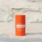 Envase en barra dōTERRA On Guard Stick con Equinácea en pie sobre tejido con fondo de pared de piedra clara.